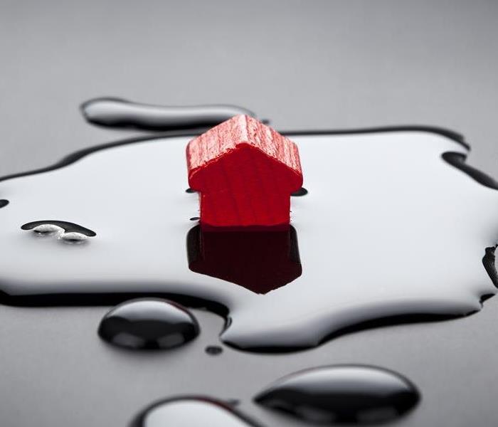A red house sitting in a puddle of water on a black surface. 